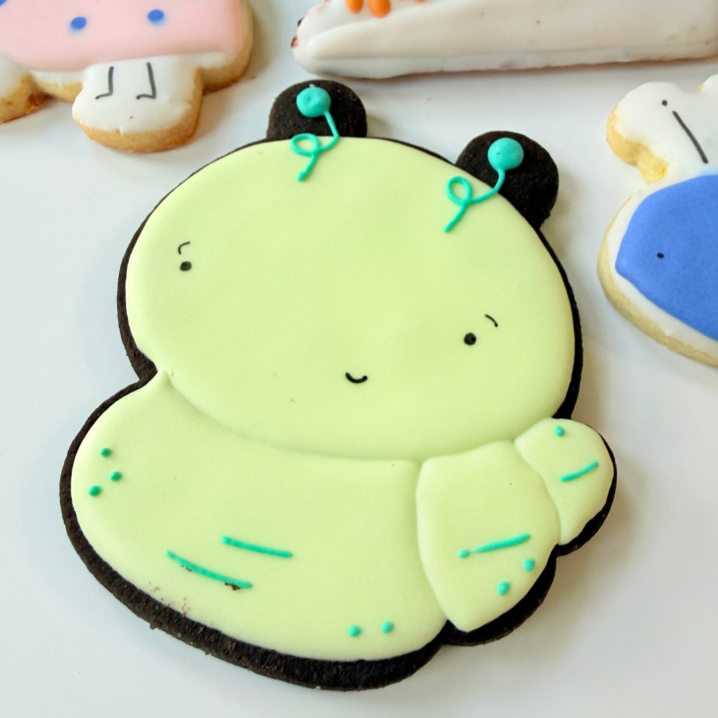 Dark chocolate cutout cookie decorated like a caterpillar in a light green color with teal antennae.